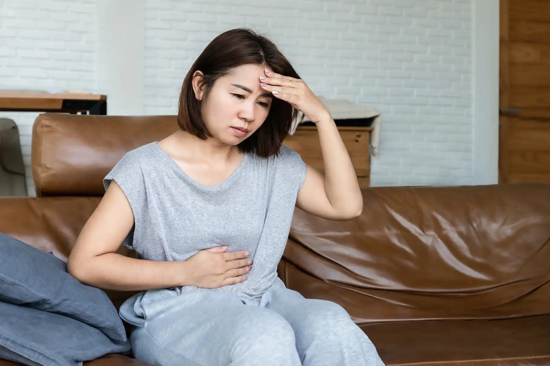 A woman holds her head and rubs her stomach in pain