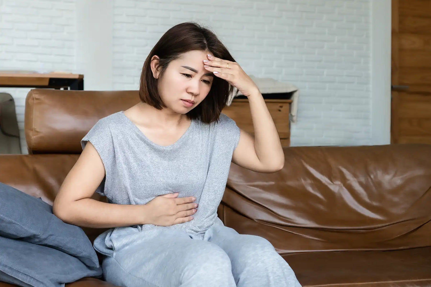 A woman holds her head and rubs her stomach in pain